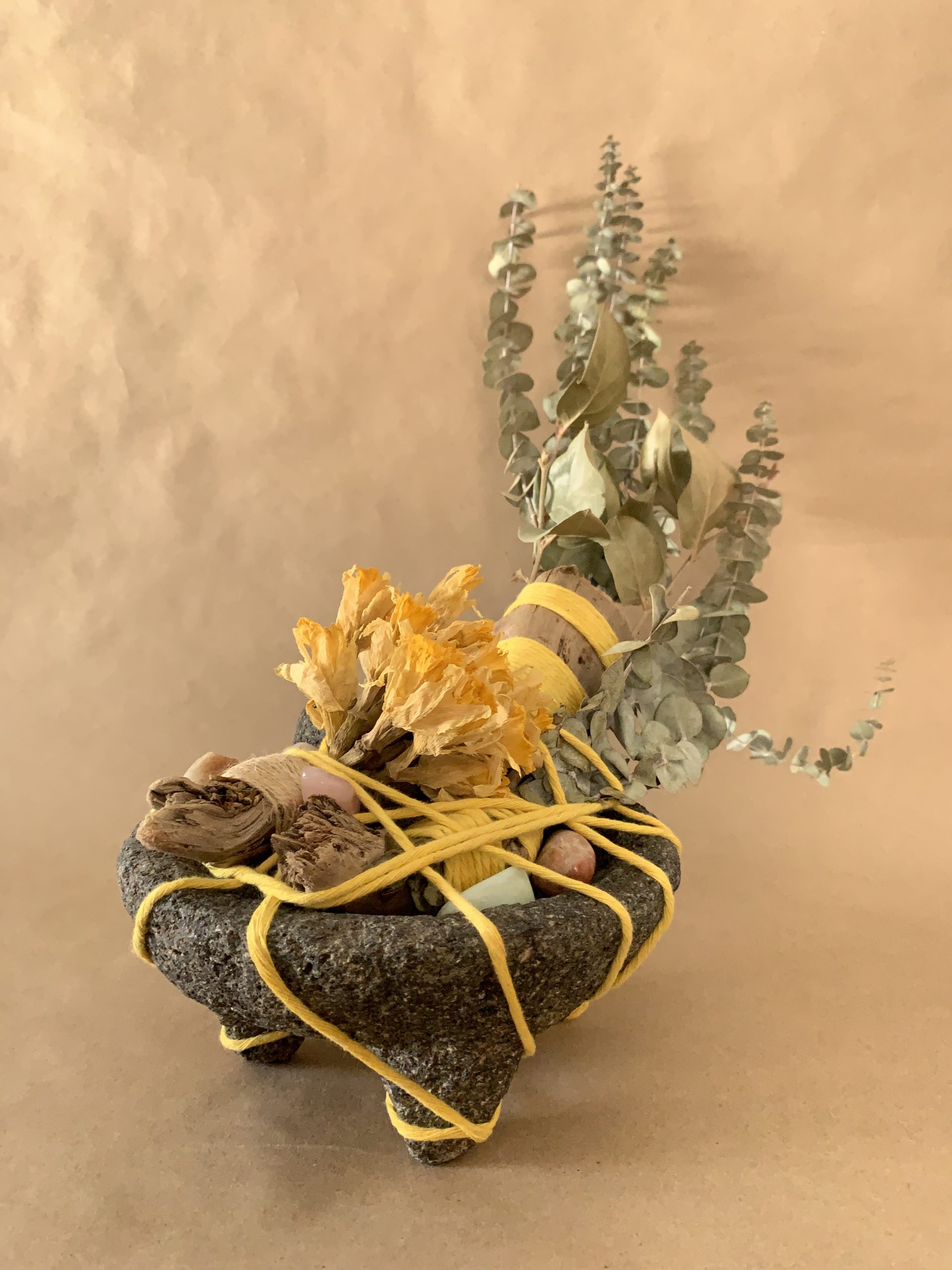 botanicals and driftwood tied with string inside of a mortar and pestle